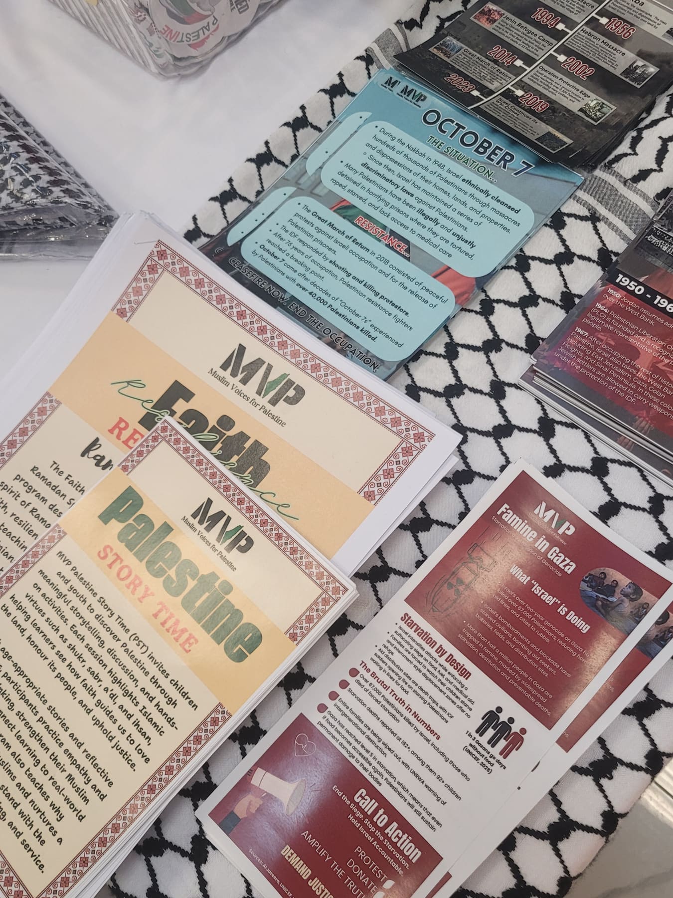 MVP flyers on a keffiyeh: Faith & Resistance, Palestine Story Time, an October 7 fact card, and a Famine in Gaza sheet