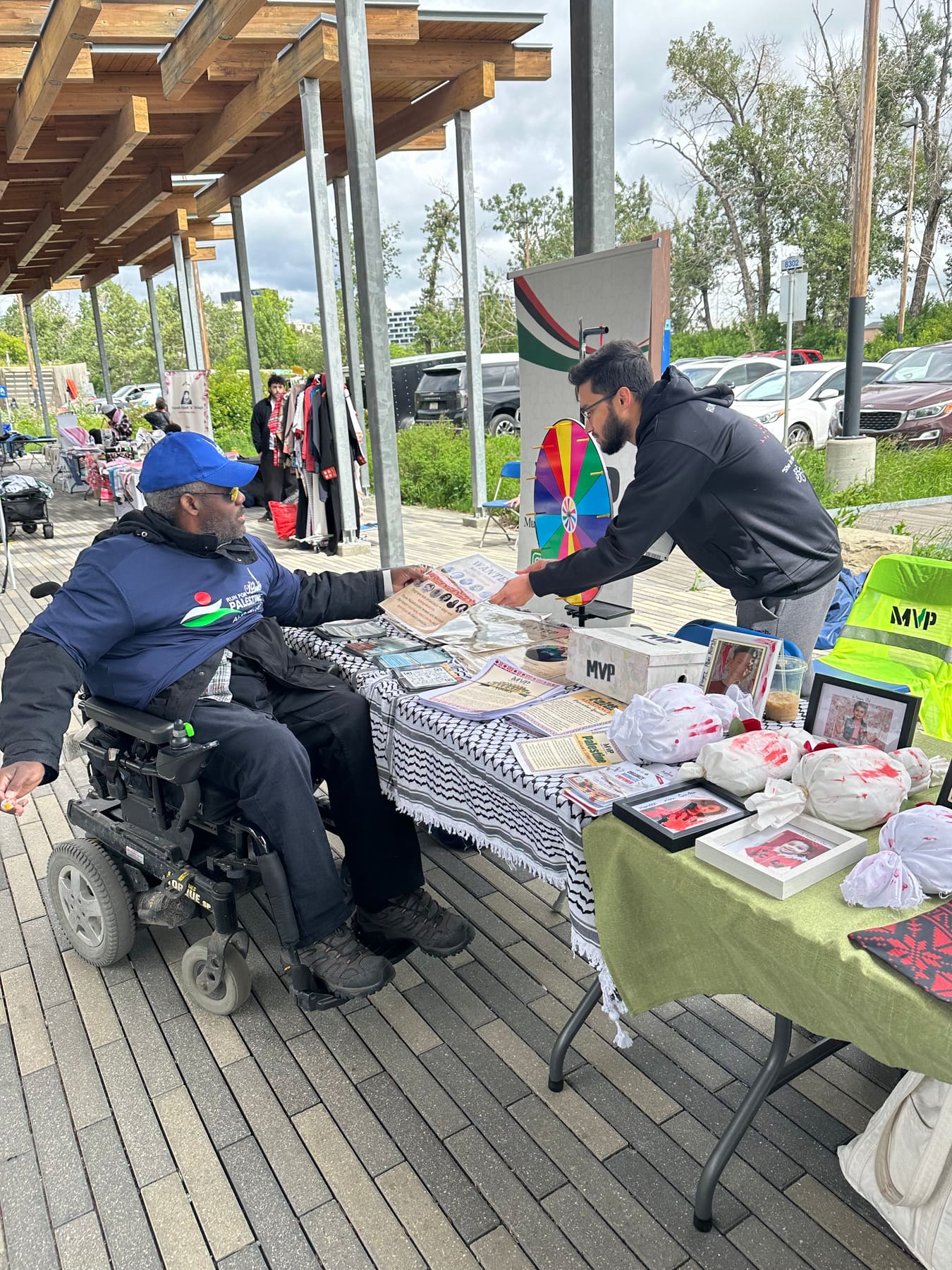 A volunteer hands a flyer to a visitor in a wheelchair at the MVP vendor booth at Run for Palestine