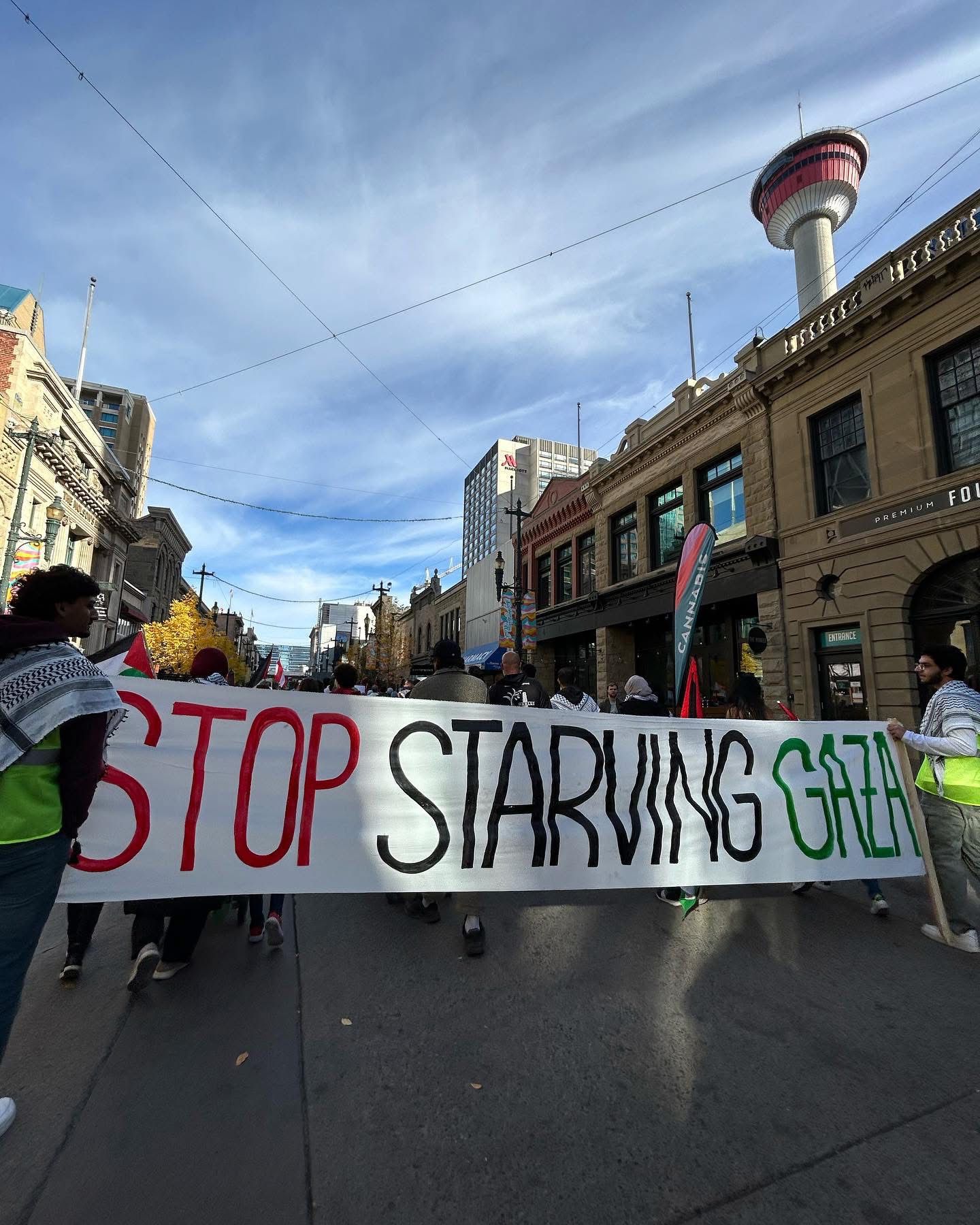 Marchers carrying a “Stop Starving Gaza” banner past the Calgary Tower