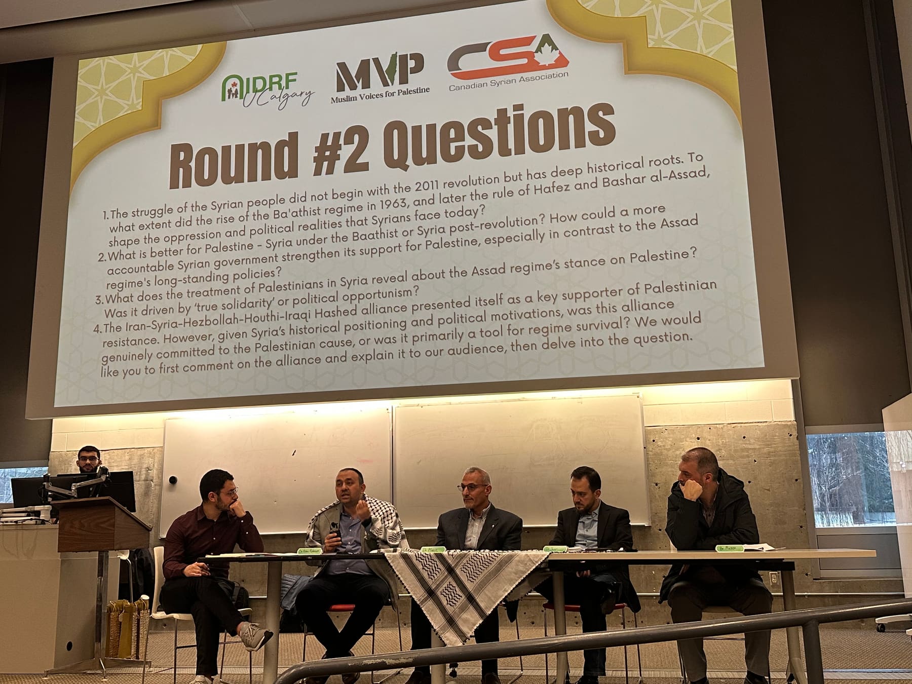 Panelists take audience questions beneath a “Round #2 Questions” slide at the From Syria to Palestine event