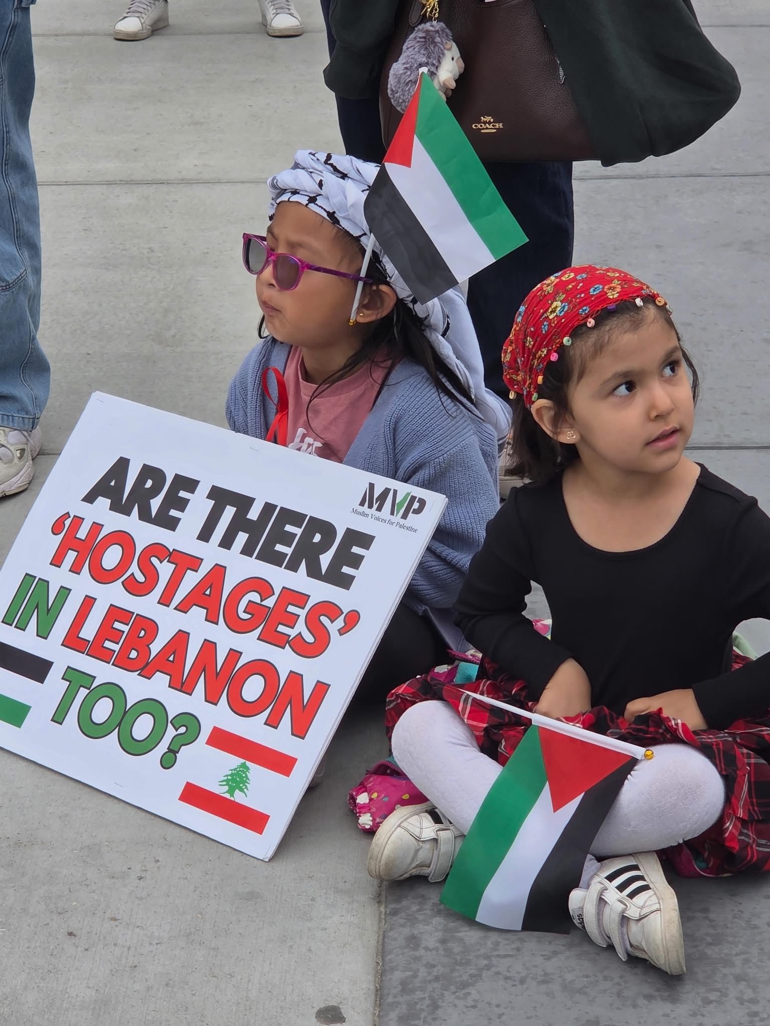 Two children at an MVP Calgary demonstration, one holding a sign and a Palestinian flag